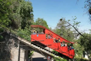 Funicular rojo con pasajeros subiendo por la pendiente rodeado de vegetación en el Cerro San Cristóbal operado por TEM Turistik.