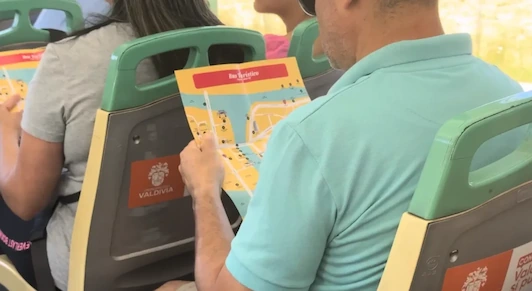 Pasajeros en un bus turístico de Valdivia miran un mapa colorido del recorrido mientras viajan.