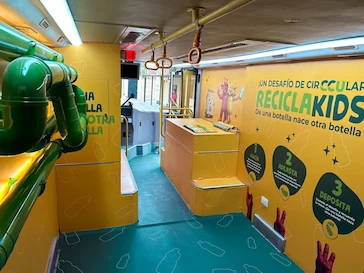 Interior del bus ReciclaKids de TEM Turistik con paredes amarillas, tuberías verdes y señalética educativa sobre reciclaje.