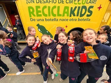 Grupo de niñas escolares sonríen sosteniendo botellas plásticas frente al bus amarillo ReciclaKids de TEM Turistik.