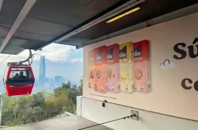 Cabina roja de teleférico en movimiento con la ciudad y el horizonte de fondo junto a un letrero publicitario en TEM Turistik.