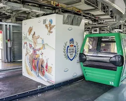 Cabina verde de teleférico en la estación junto a una pared ilustrada con temática de Red Bull Soapbox Race en TEM Turistik.