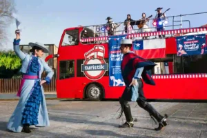 Pareja de bailarines con vestimenta tradicional chilena bailando cueca frente a un autobús rojo de TEM Turistik con músicos en vivo.
