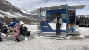 Módulo móvil de Pucón de TEM Turistik en zona nevada con una promotora y personas sentadas en mesa de picnic.