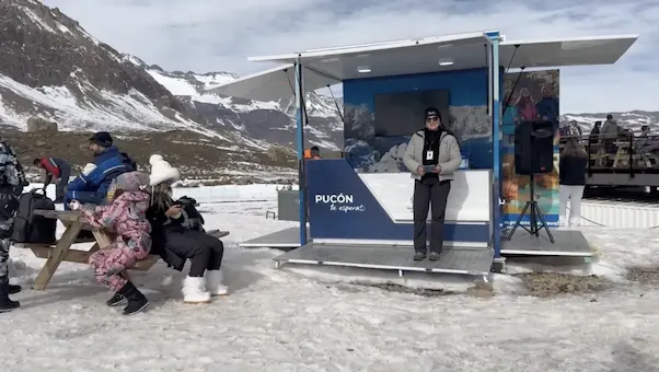 Módulo móvil de Pucón de TEM Turistik en zona nevada con una promotora y personas sentadas en mesa de picnic.