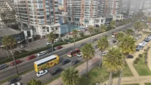 Vista aérea de un bus de dos pisos amarillo de TEM Turistik circulando por una avenida costera con palmeras y edificios altos.