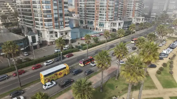 Vista aérea de un bus de dos pisos amarillo de TEM Turistik circulando por una avenida costera con palmeras y edificios altos.